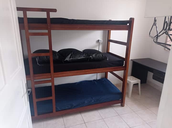 Spavaća soba s rešetkama, vješalicama, radnim stolom  i ventilatorom.