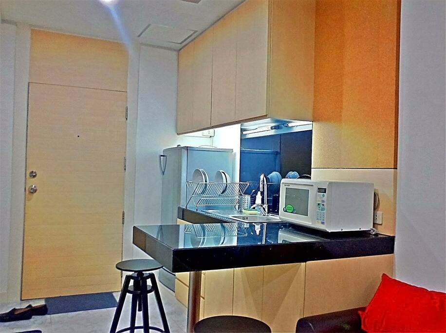 Mini kitchen with utensils, plates, glasses, microwave and refrigerator. Good for heating up take away food.