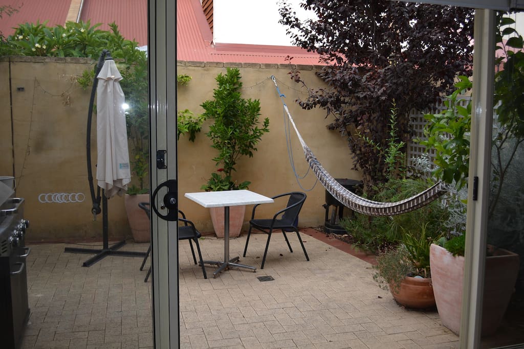 The lounge spills onto a sunny courtyard with BBQ, outdoor setting and hammock