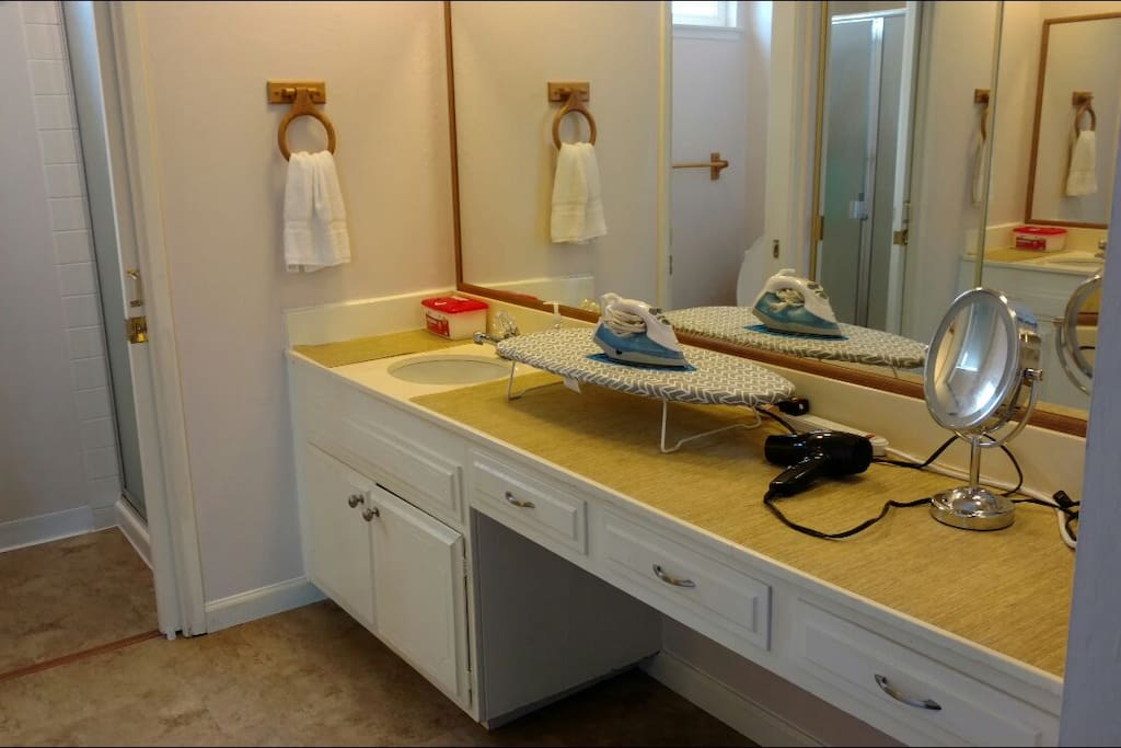 Vanity area with sink, hairdryer, lighted mirror, iron, and ironing board.