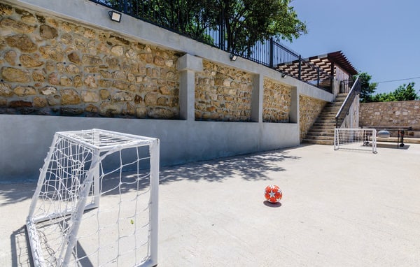 A designated play area features two small soccer goals positioned on a smooth concrete surface, with a brightly colored ball resting in between. A stone wall provides a rustic backdrop, while nearby steps lead to an upper level surrounded by greenery.