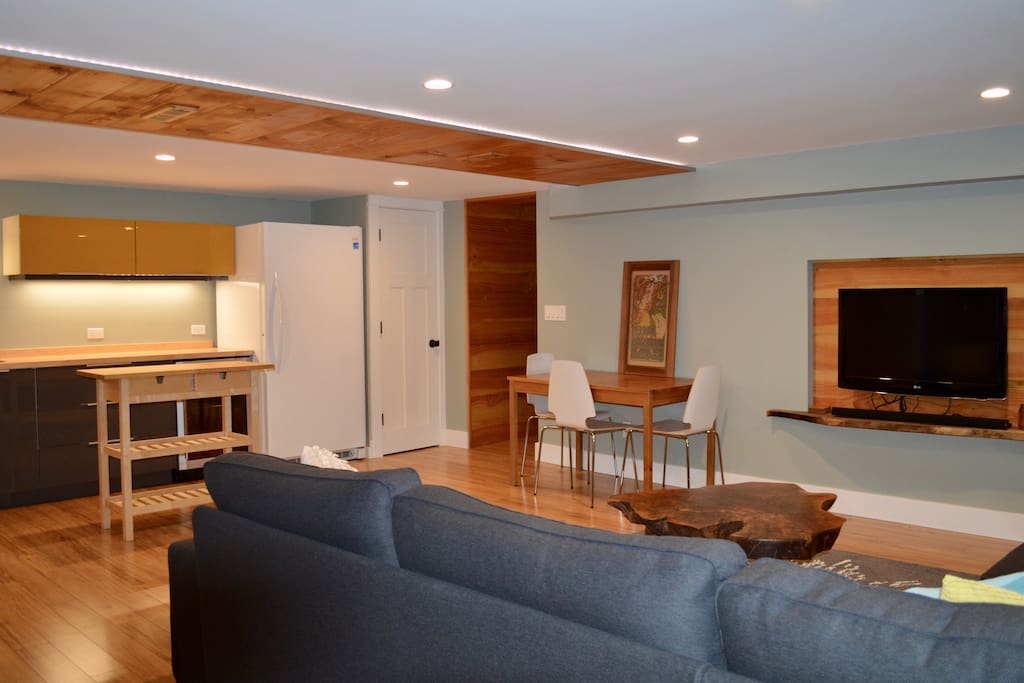 Living area with sectional couch, kitchen, dining table, suite entrance and flat screen tv complete with Apple TV featuring Netflix, Hulu Plus, and more!