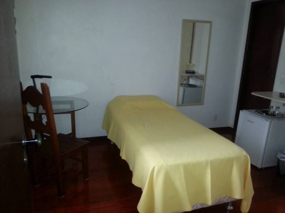 Quarto arrumado para 1 hóspede com mesinha e luminária