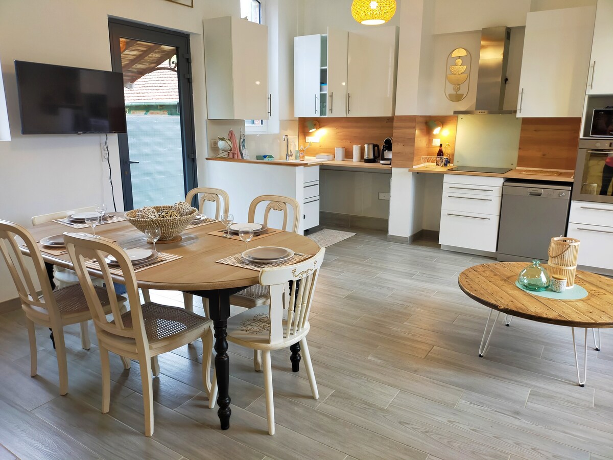 A bright dining area features a wooden table surrounded by six chairs, complemented by a modern coffee table in the center. The open kitchen is equipped with sleek cabinetry, a range oven, and a display space for kitchen items, creating an inviting communal space.