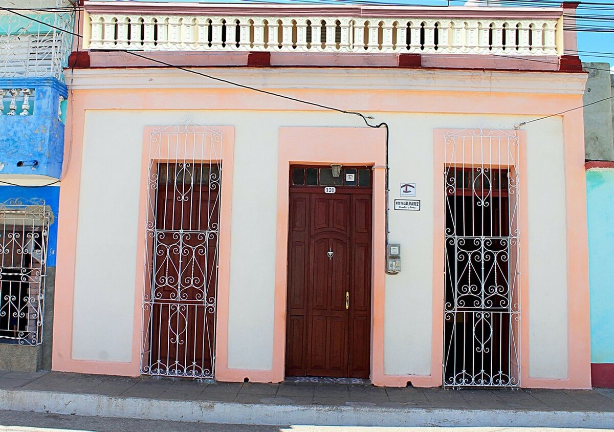 The exterior of the hostal features a classic facade with a wooden front door framed by decorative ironwork. Two large windows are also adorned with similar iron grilles, adding to the property's charm. The light-colored walls are complemented by subtle pastel accents.
