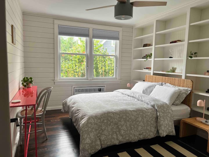 2nd bedroom features a Queen bedroom with bookcases filled with classic novels, plants and plush bedding. Ceiling fan, rattan furnishings and modern pink enamelled workstation and room for an optional crib. Closet with ample storage. 