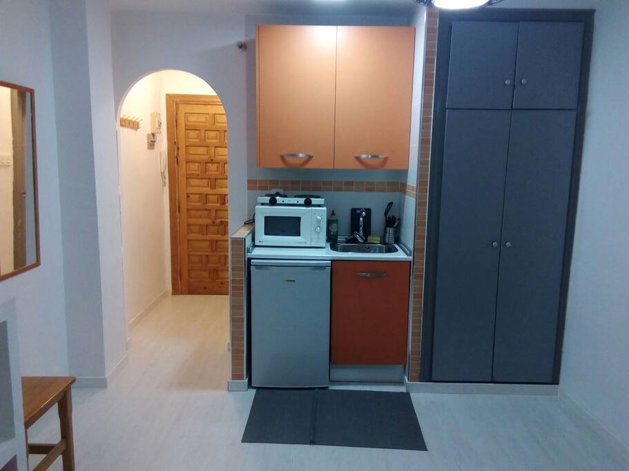 Cocina con nevera, armario con enseres de cocina, fregadero y microondas