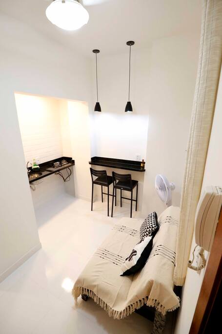 Entrada da casa. Sala com sofá, bancada para refeições e cozinha.