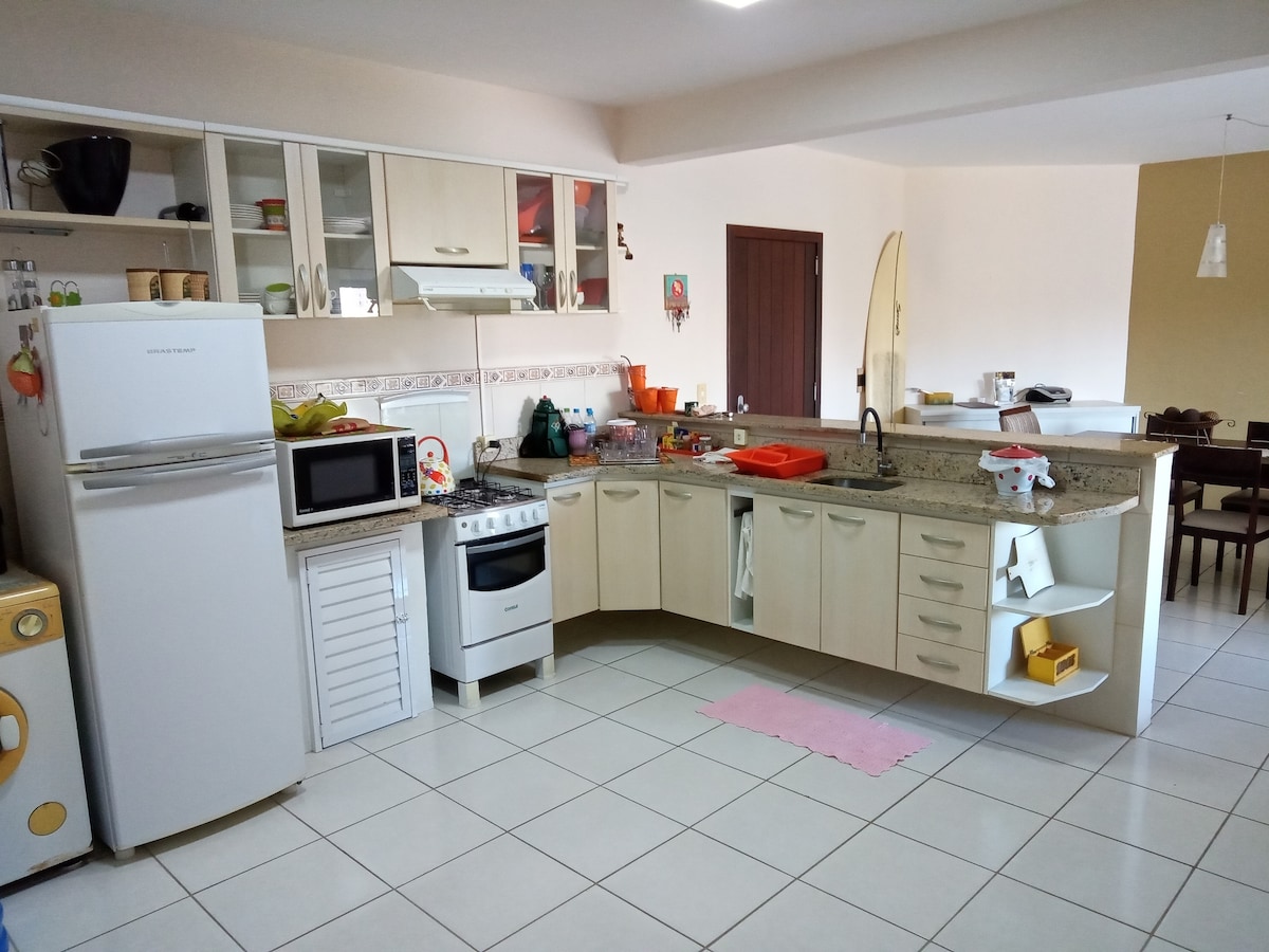 A functional kitchen is showcased with light granite countertops and a white tile floor. Storage cabinets line the walls, featuring a stove, microwave, and refrigerator. An open layout connects to the dining area, visible on the right, with multiple chairs and a table, inviting communal dining.