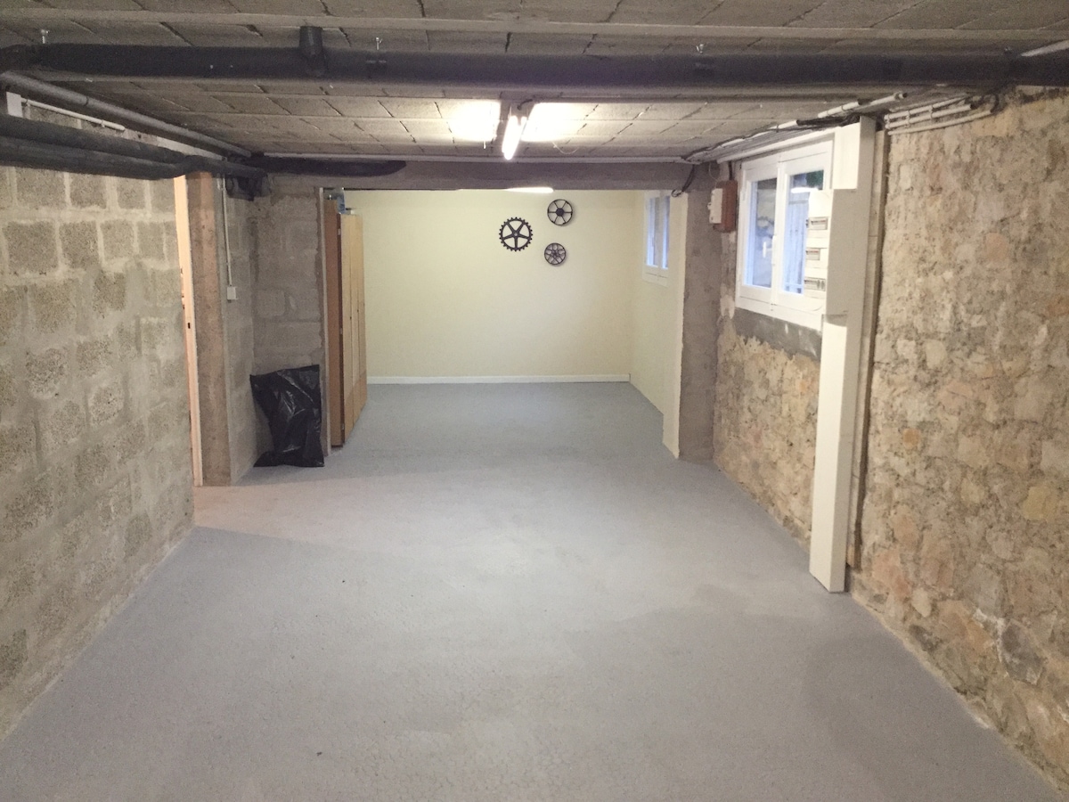 A spacious garage is depicted, featuring a smooth concrete floor and exposed stone walls. Light fixtures illuminate the area, while a few decorative items are mounted on one wall. A black bag sits in the corner, contributing to the overall organized atmosphere.