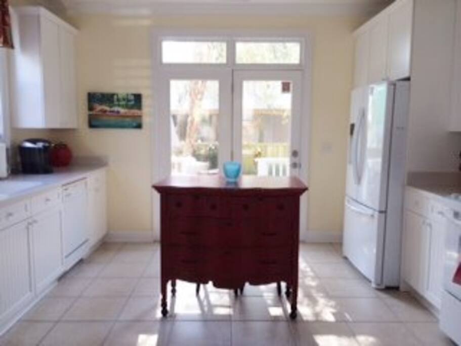 Spacious well lit kitchen with white cabinets, custom back splash and counter-tops and RED accents.