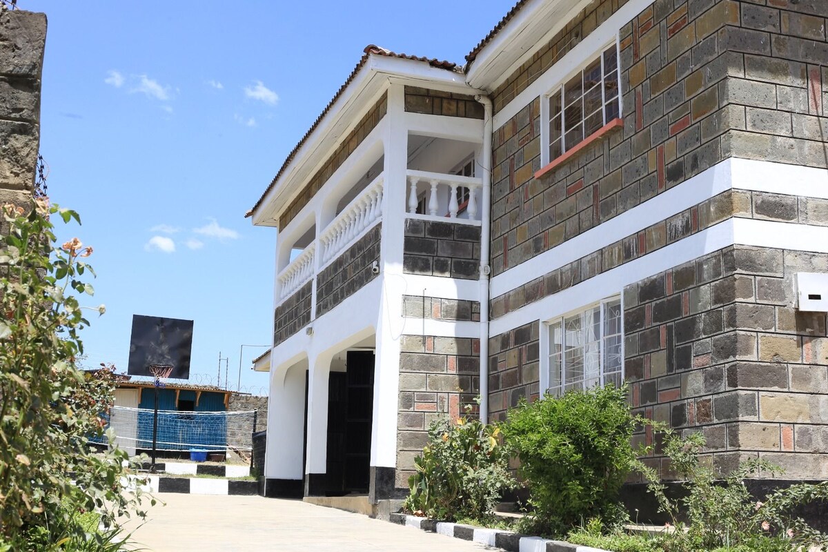 The exterior of a two-story building is shown, featuring a combination of stone and white walls. A balcony adds character to the upper floor, while a landscaped area with greenery is visible in the foreground, enhancing the inviting appearance of the property.