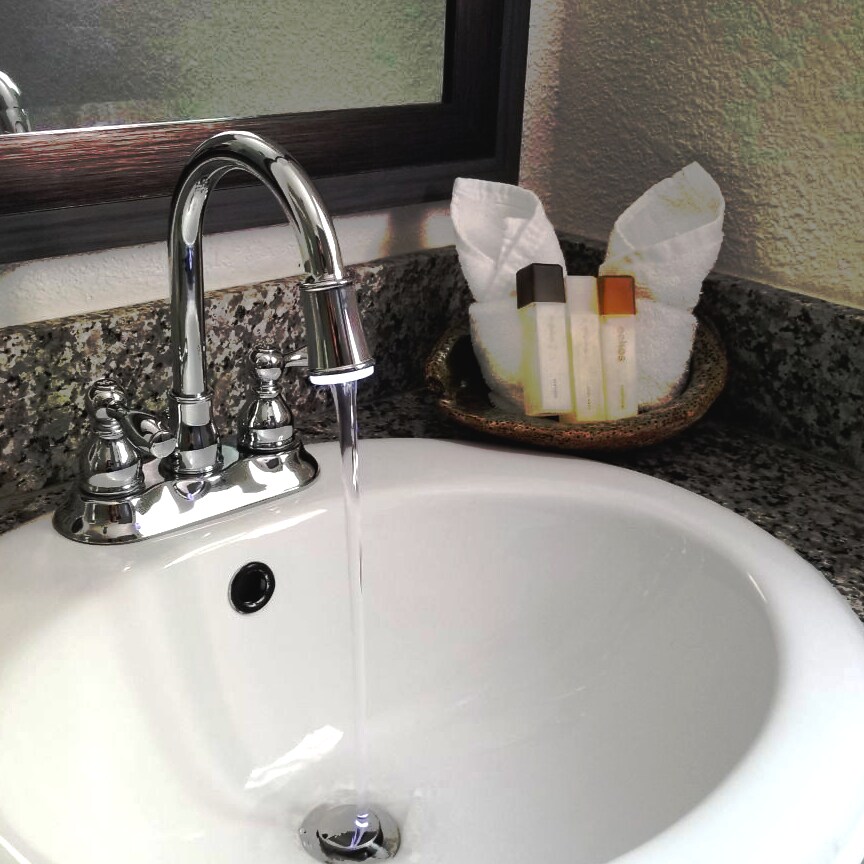 A modern bathroom sink features a polished chrome faucet with water flowing into the white basin. A small dish nearby holds neatly arranged toiletries and soft towels, while the granite countertop adds a touch of elegance.