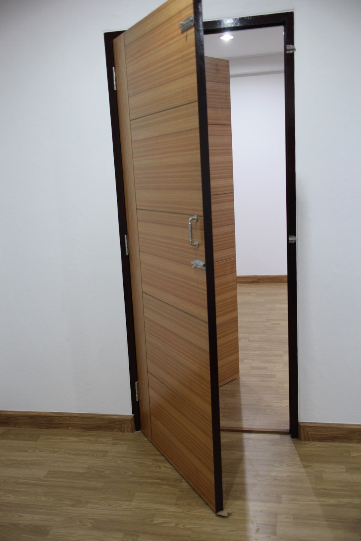 A wooden door with a sleek design is partially open, revealing a glimpse of the interior space. Light wooden flooring is visible beyond the doorframe, contributing to a clean and contemporary aesthetic.