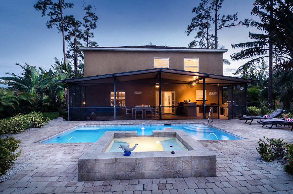 A serene outdoor space showcases a private pool complemented by a hot tub, surrounded by lush greenery. A covered patio with direct access to the kitchen stands in the background, inviting relaxation and outdoor dining. The tranquil atmosphere is enhanced by the evening sky.