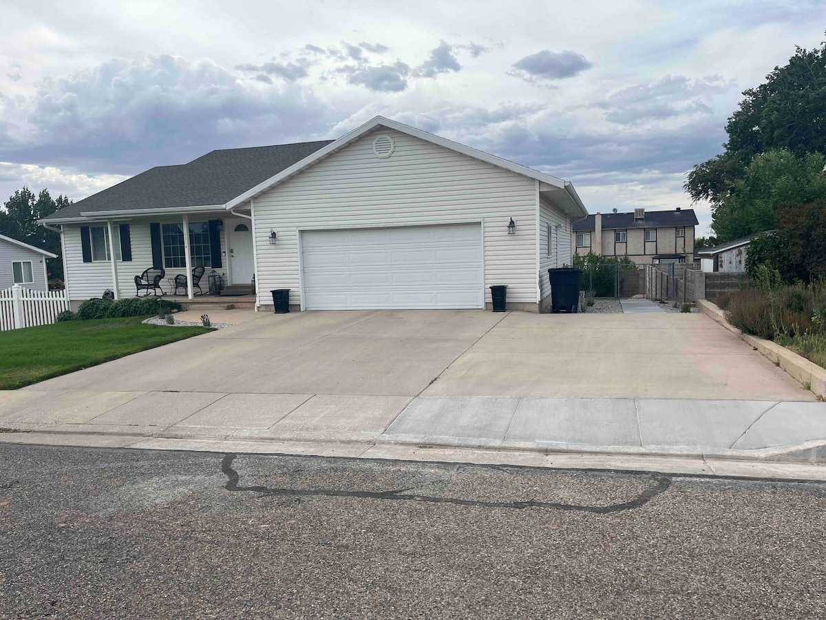 A welcoming exterior view of the home showcases a large driveway leading to a two-car garage. The house features a front porch with seating and a neatly landscaped yard. Gray clouds appear overhead, hinting at a serene, suburban atmosphere.