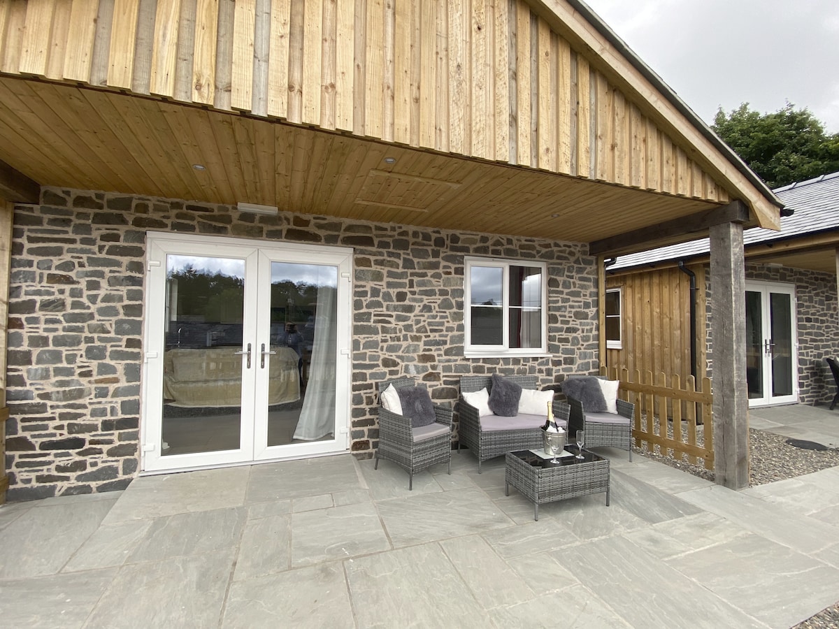 An outdoor patio area features woven seating with plush cushions, inviting relaxation. A stone wall provides texture alongside light-colored flooring. Glass doors lead into the lodge, enhancing the connection between indoor and outdoor spaces.
