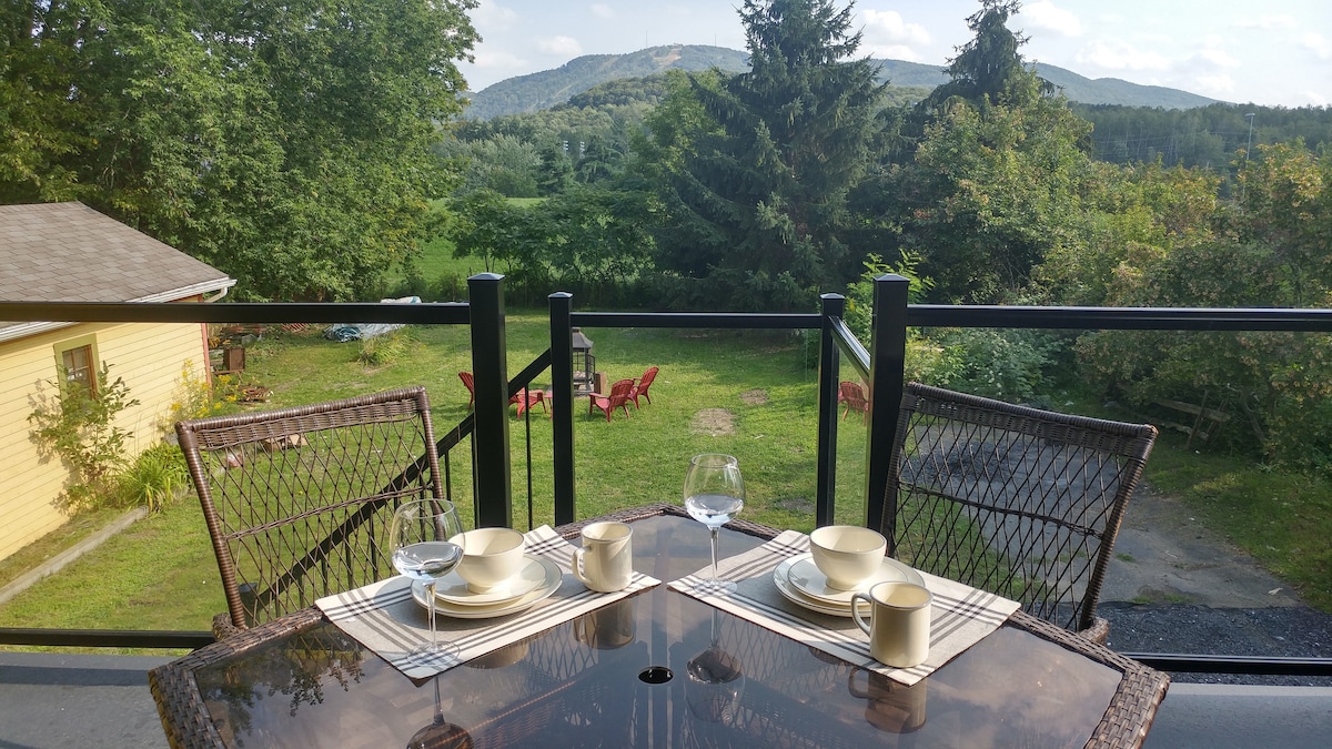 A private terrace features a round dining table set for two, with dishes and glasses arranged neatly. The background showcases a lush green landscape and distant mountains, providing a tranquil setting for outdoor dining.