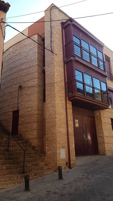 Exterior de la casa. Se accede por las escaleras. La casa tiene un enorme ventanal en ambas plantas.
