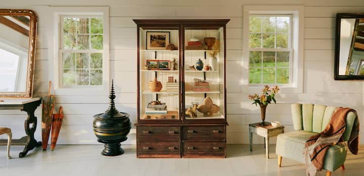 Une photo montre un grand salon blanc abritant une collection de meubles anciens, dont une grande vitrine en bois et en verre remplie d'antiquités de valeur.