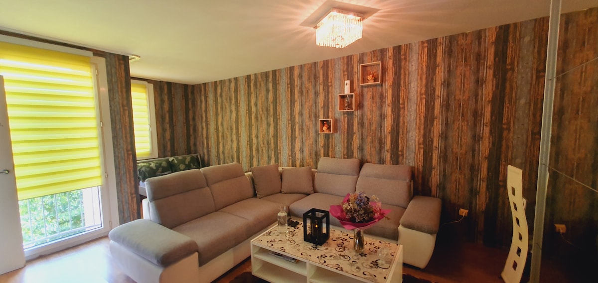 A modern living area showcases a comfortable sectional sofa paired with a decorative coffee table. The walls feature a textured design, while vibrant yellow window coverings allow natural light to fill the space. A few framed pictures are displayed, adding a personal touch.