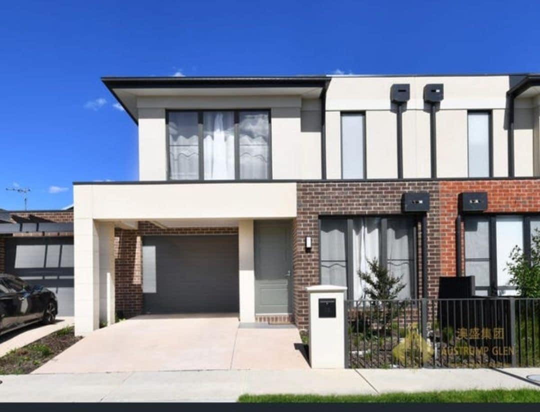 The contemporary two-story home features a well-maintained exterior with a mix of brick and rendered walls. Large windows allow natural light to fill the space. A pavement leads to a garage, with greenery visible in the landscaped area.