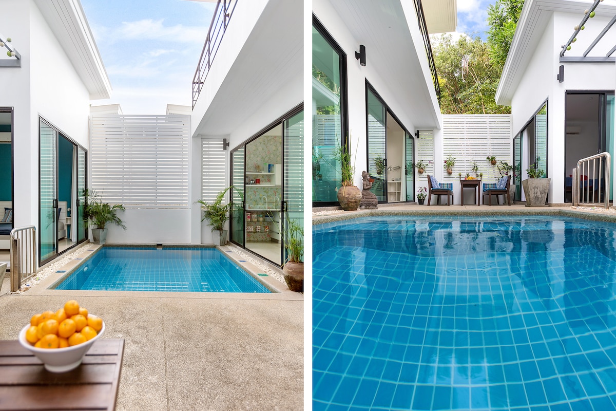 A tranquil courtyard features a clear blue pool surrounded by modern architecture. Large sliding doors offer easy access to the outdoors, while potted plants add greenery. A patio area with a table and chairs provides a space for relaxation and socializing.