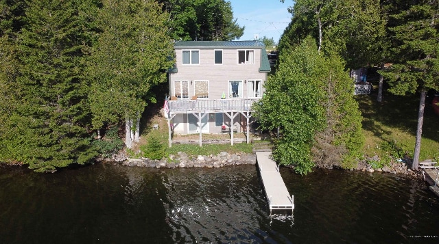 A two-story home stands gracefully by the water's edge, framed by lush greenery. A dock extends into the lake, providing easy access for water activities. The exterior features a mix of wood and siding, with large windows inviting natural light.