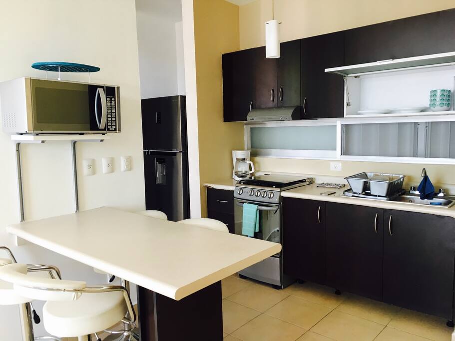 Cocina equipada con refrigerador grande, con dispensador de agua fría y congelador, estufa con horno, microondas y equipo de cocina.