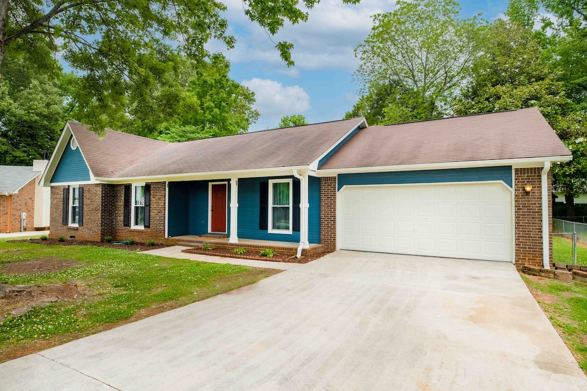 A charming single-story home is presented with a blue and brick facade, set on a quiet street. The front porch features a warm entrance, complemented by well-maintained landscaping. A spacious driveway leads to a two-car garage, creating a welcoming curb appeal.