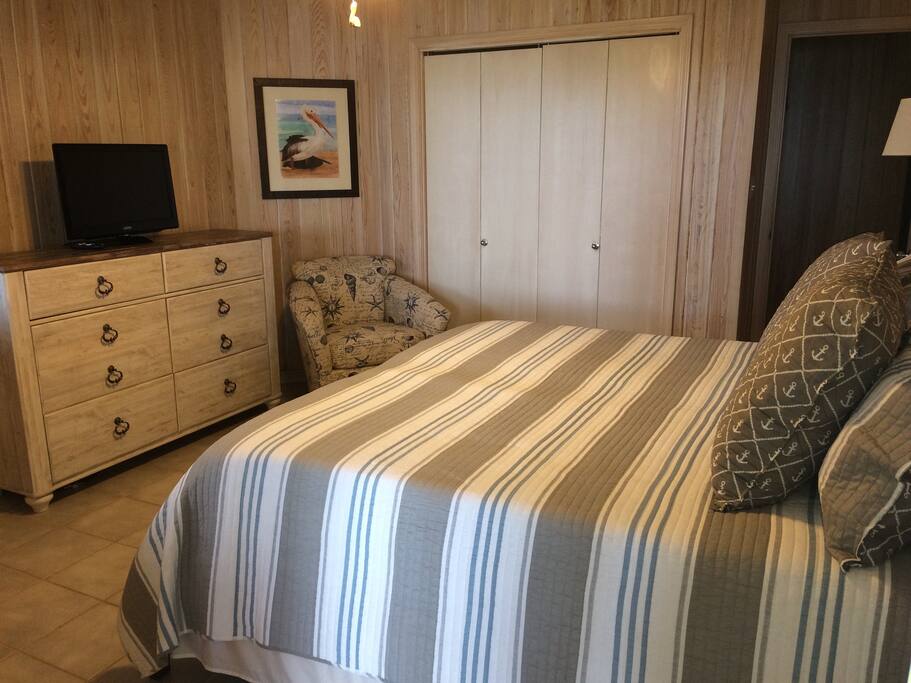 Private bedroom with king size bed, large dresser, sitting chair, and ample closet space with hangers.
