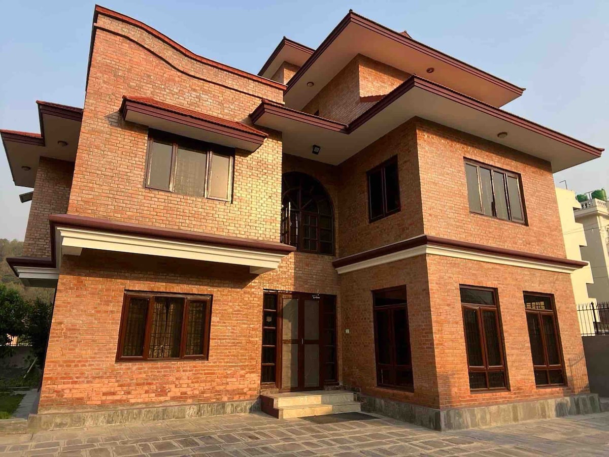 The exterior of a newly built house is presented, featuring a combination of brick and modern architectural elements. Large windows allow for ample natural light, while the entrance is marked by a set of steps leading to double doors. The surrounding space is paved with stone.