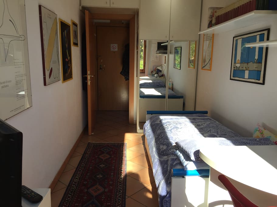 Davanti al letto, l'armadio bianco a specchio circonda la porta di entrata. a dx si intravede la scrivania, a sx la tv