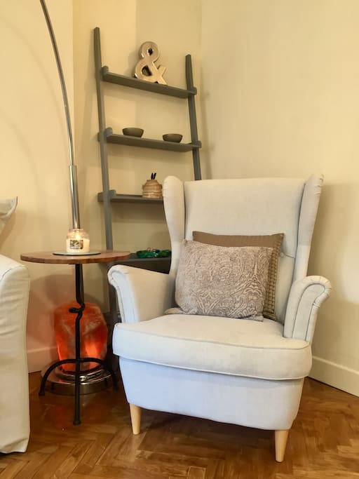 Living room corner with comfortable armchair, Himalayan salt lamp and ladder shelves with decor