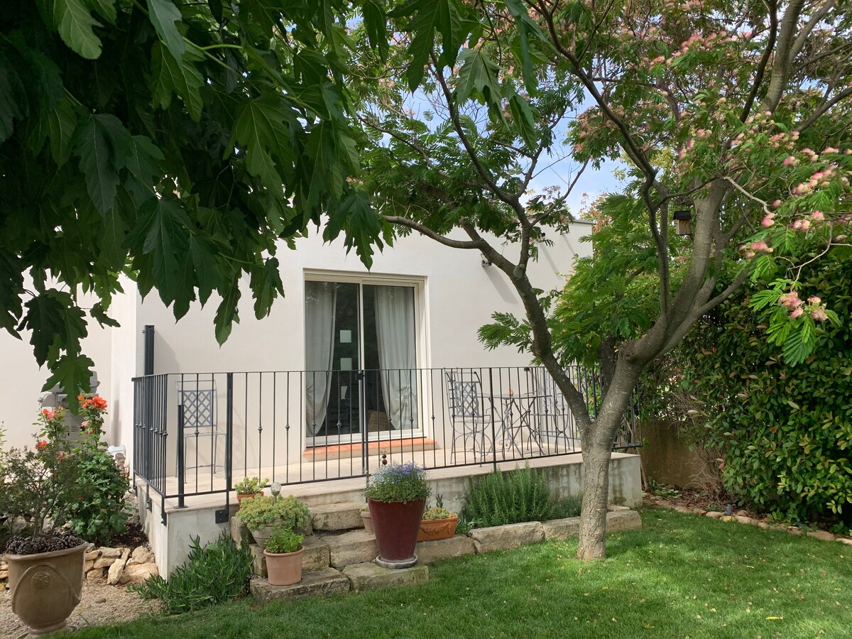 The exterior of the property features a charming terrace surrounded by greenery. A glass door leads into the living space, while potted plants and a wooden railing add to the inviting atmosphere. The grassy area provides a natural setting, enhancing the serene environment.