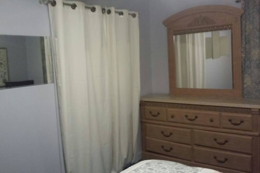 Large dresser with mirror and large closet behind drapes