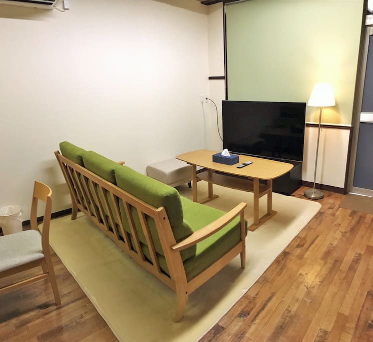 Living room with a 58-inches television, with a sofa and a cushion that allow 4-6 people to sit together.