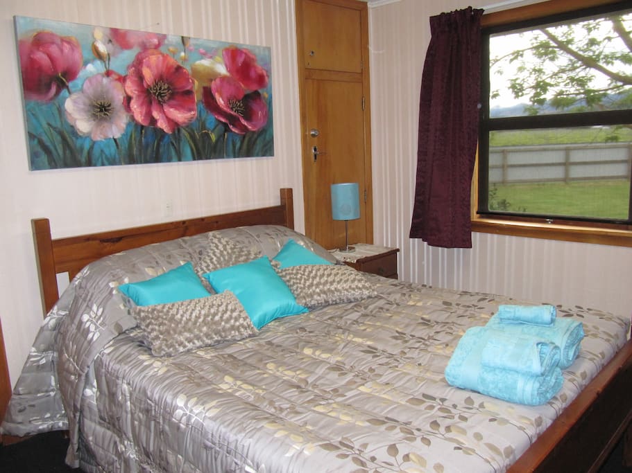 Queen bedroom with luggage rack, towel rail, el blankets, lamp