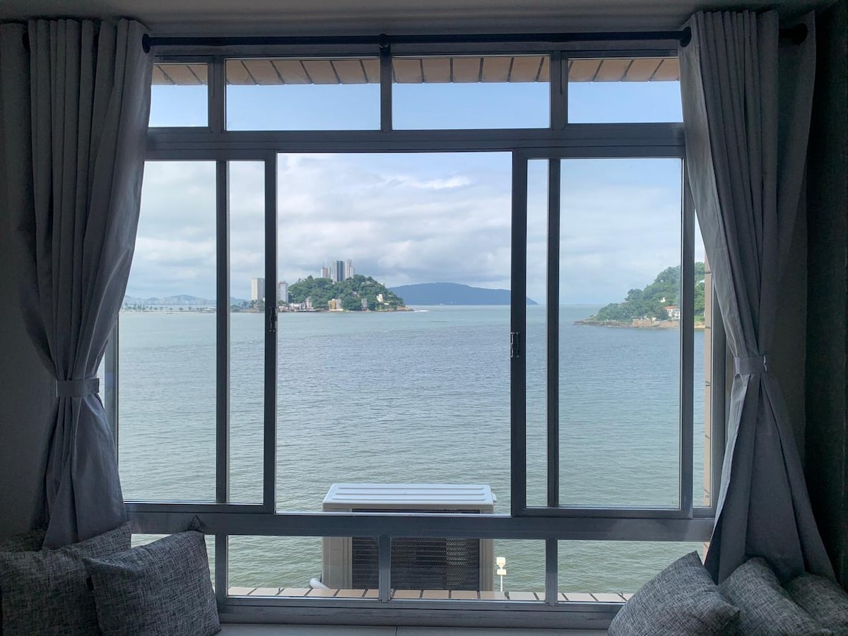 A large window displays a serene view of the bay, featuring gentle water colors and distant hills. Soft curtains frame the glass, enhancing the natural light that fills the room. The tranquil scene invites relaxation and provides a connection to the outdoor landscape.