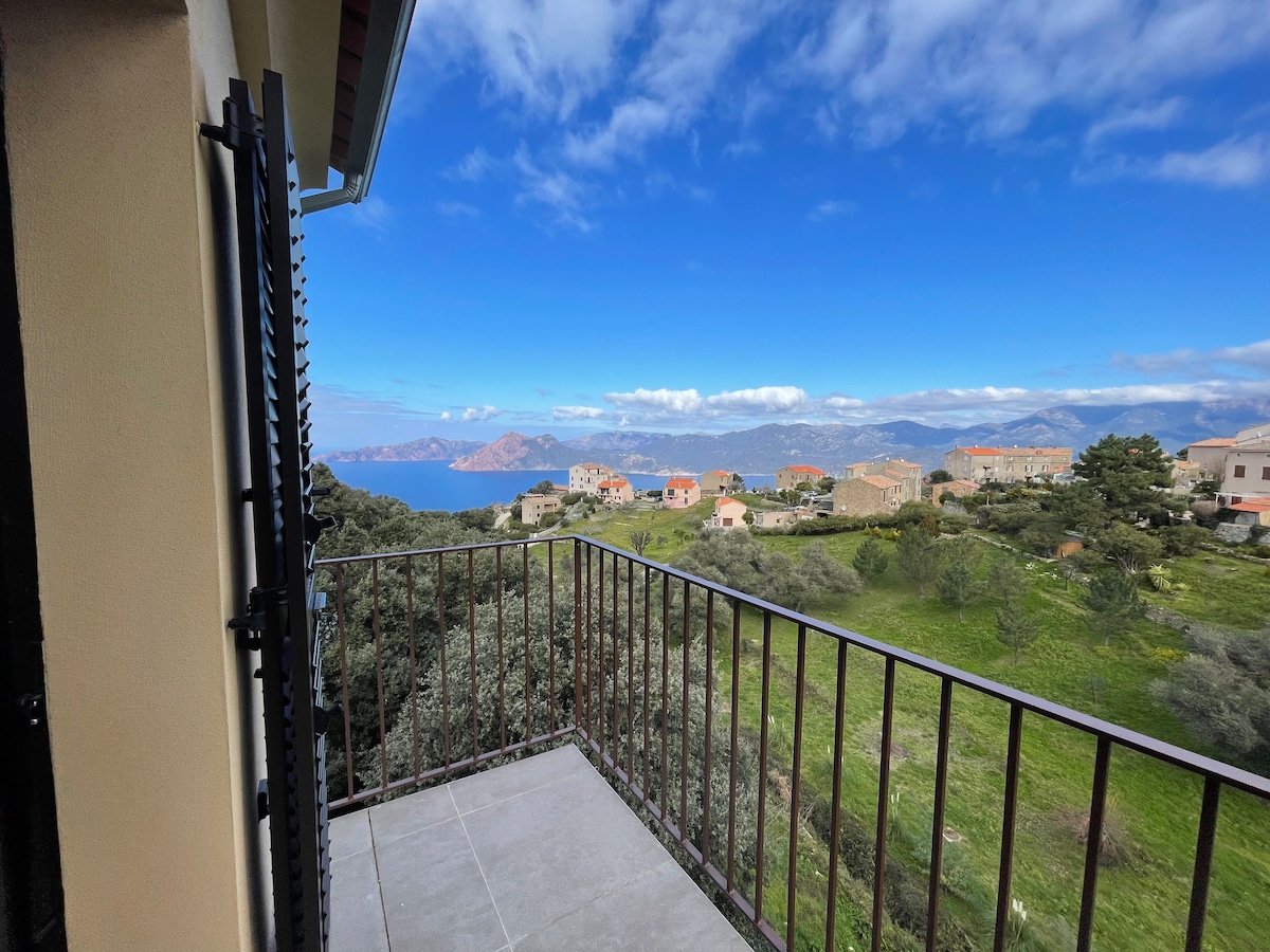 A private balcony offers a sweeping view of the surrounding landscape, showcasing green hills and distant mountains against a clear blue sky. The space features a smooth tiled surface and a wrought iron railing, allowing for an unobstructed perspective of the coastal scenery.