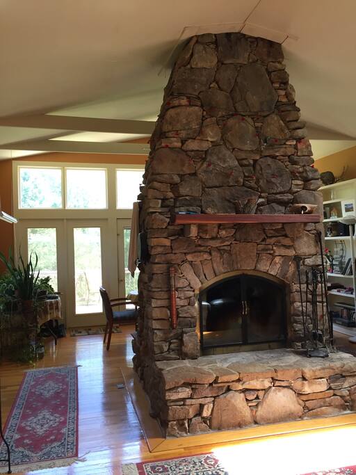 Large fireplace located beside the kitchen. Fireplace is located in the center of the room and can be enjoyed on both sides. Reading nook and comfy sofa facing one side of the fireplace and a large dinner table (seats 8+) with scenic views on the other side of the fireplace. Plenty of work space if needed. Attached are 2 porches for enjoying morning coffee with nature or just a quick dip or a long soothing sit in the hot tub. Fireplace is not permitted to use by guests.