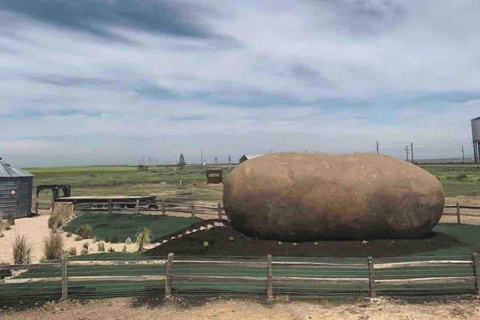 Boise Potato Hotel, a potato-shaped lodging in a flat green landscape with farmland underneath overcast sky.