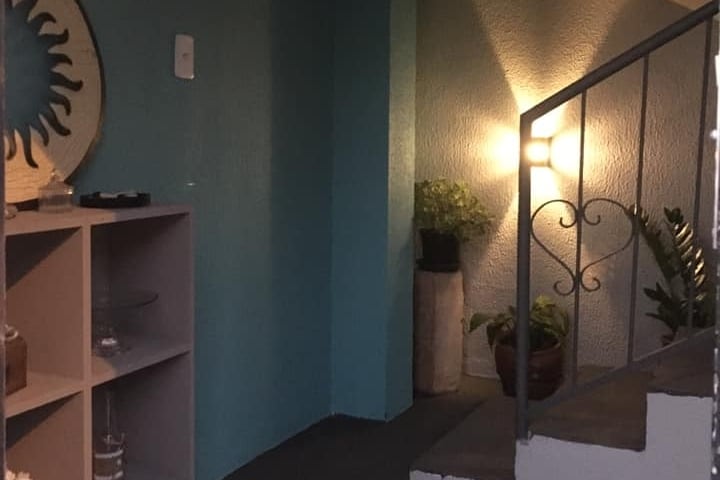 A well-lit corner of the space features a staircase with a decorative railing, leading to a serene area. A potted plant adds a touch of greenery, while the turquoise wall reflects natural light, creating a calm atmosphere. A shelf is positioned nearby, providing display space.
