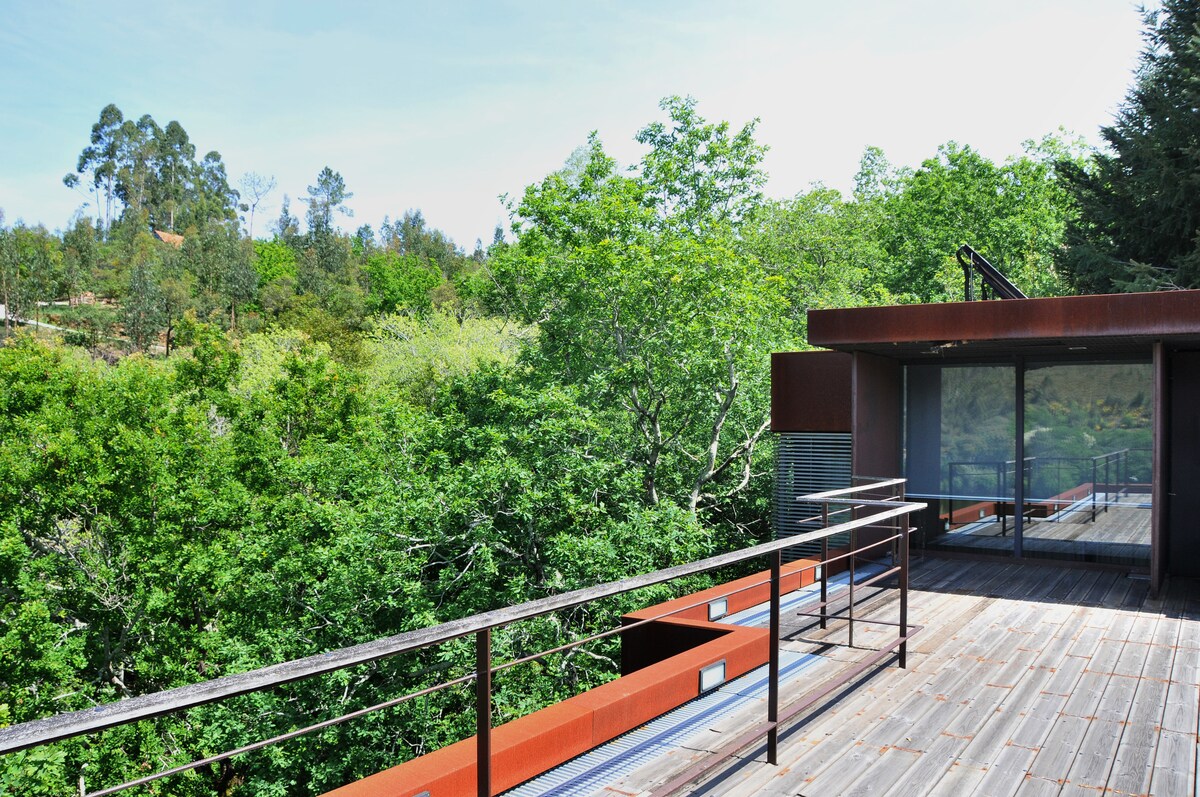 A spacious terrace offers views of lush greenery surrounding the property. The wooden decking is complemented by a railing for safety. Large glass doors lead to the interior, integrating outside and inside spaces seamlessly.