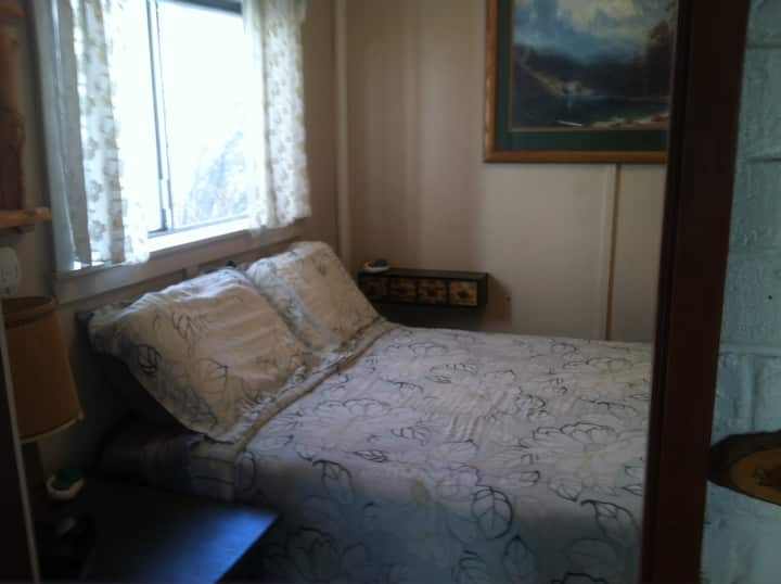 Small bedroom fits a double bed and small closet with hangers and dresser.
