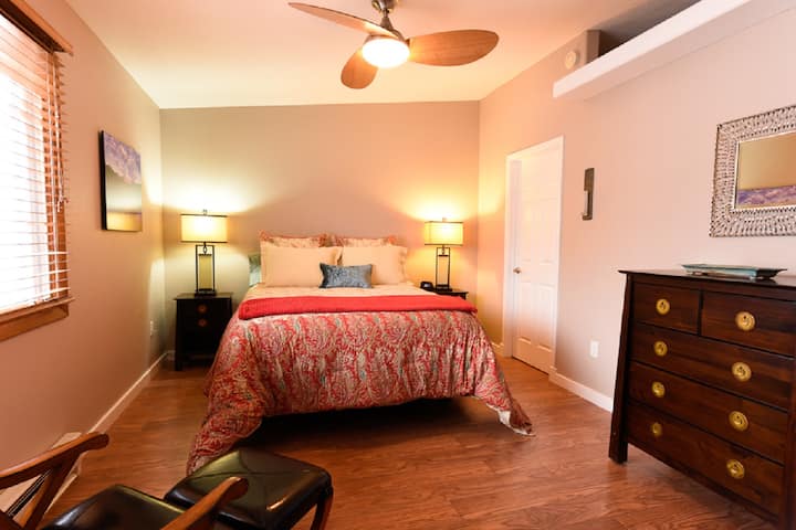 Dormitorio con sábanas de lujo, silla de cuero, vestidor y ventilador de techo. 