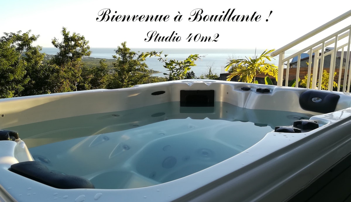 A private hot tub is displayed on a terrace, positioned to overlook the Caribbean Sea and surrounding greenery. The tub features several seats and is filled with clear water. Lush tropical plants frame the area, enhancing the serene ambiance.