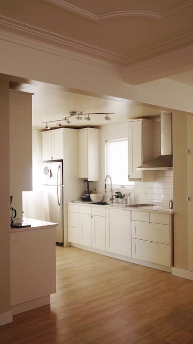 Kitchen with white cabinets, quartz countertop dishwasher, microwave, oven, coffee machine, stovetop, ninja blender, toaster.