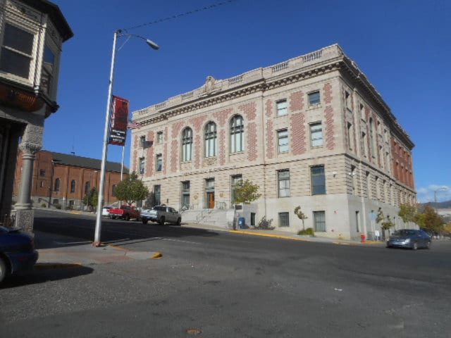 A historic building is prominently displayed across the street, featuring elegant architectural details with a mix of brick and stone. Large windows are arranged symmetrically on the façade, and a clear blue sky serves as a backdrop.