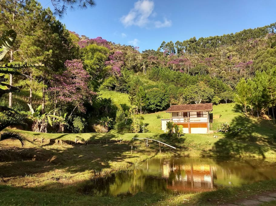 Vista frontal do chalé, lagoa e mata.
